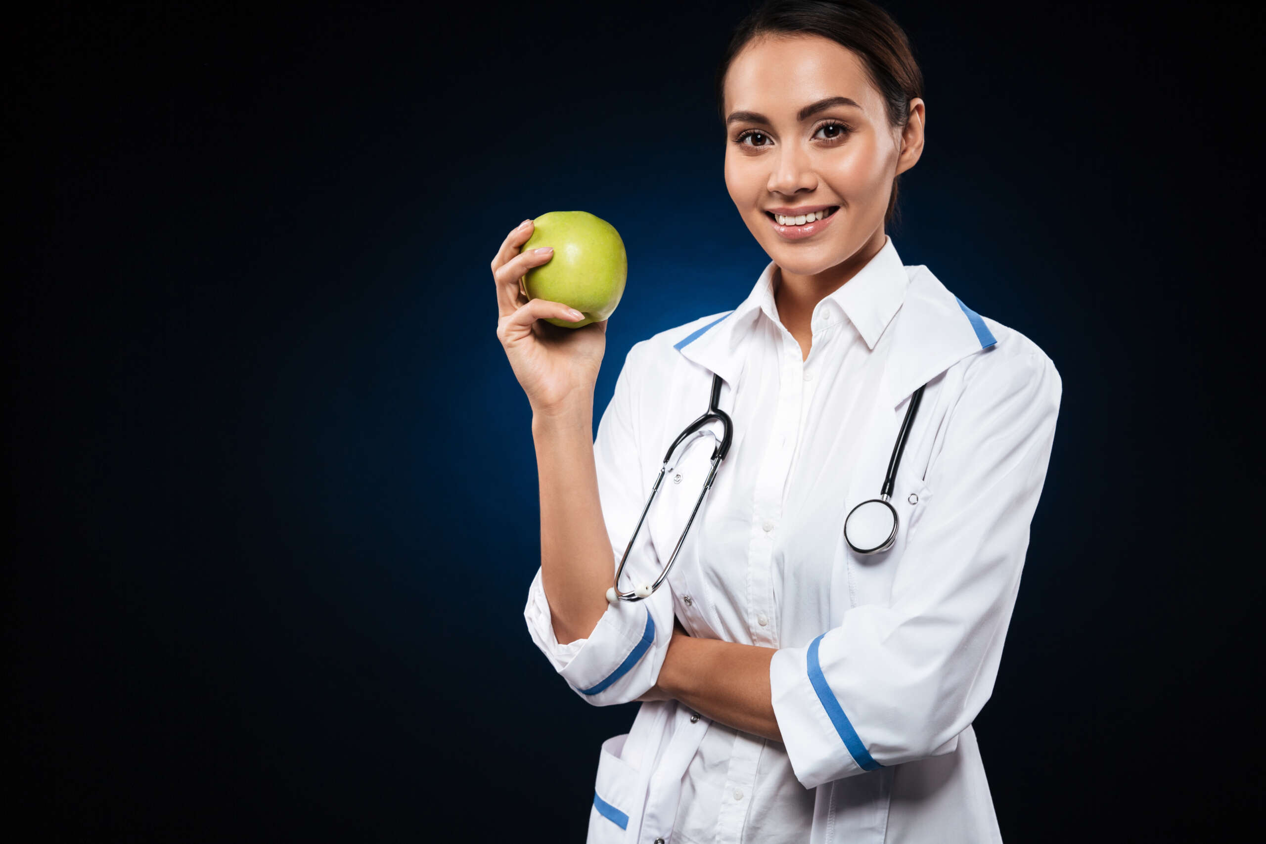 Young smiling female doctor holding a bowl of fresh fruit, promoting healthy eating and weight loss.