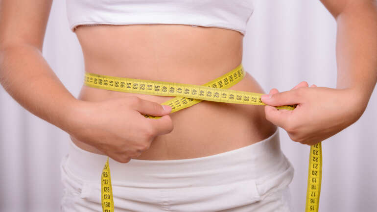 Woman measuring her waistline to track fitness and prevent obesity.